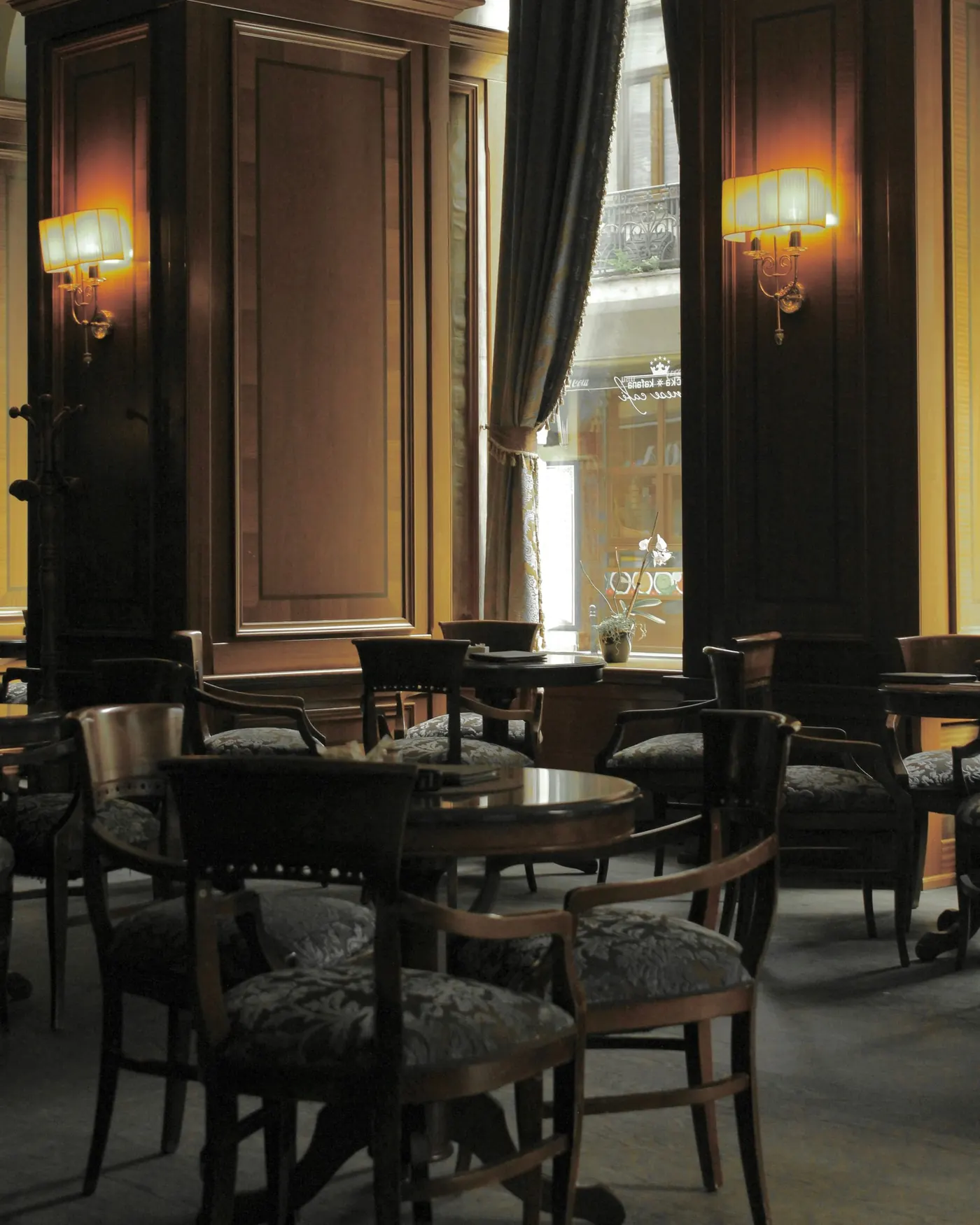 Klassisch-nostalgisches Kaffeehaus-Interieur mit warmen Wandleuchten und Kleiderständern zwischen den Tischen
